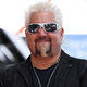 Guy Fieri in sunglasses and a black jacket, smiling